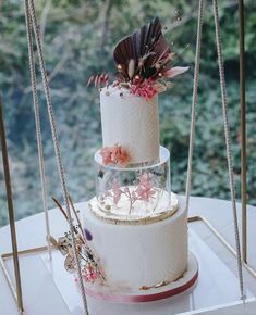 a three tiered white cake with pink flowers on top is sitting on a table