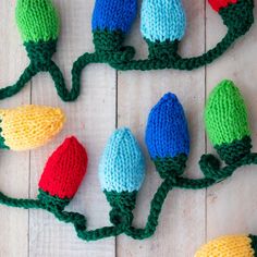 crocheted christmas lights are displayed on a wooden surface with green stems and red bulbs