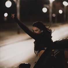 a woman sitting on the hood of a car with her arms up in the air