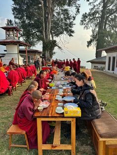 a group of people sitting at a long table eating food and drinking water from bowls