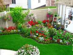 a garden with lots of flowers and plants in the grass next to a fenced yard