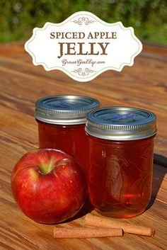 two jars of apple jelly sit on a table next to an apple and cinnamon stick