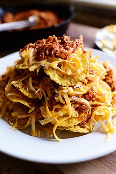 a white plate topped with nachos covered in cheese and chili sauce on top of a wooden table