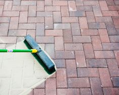 a mop laying on the ground next to a brick walkway with a green handle