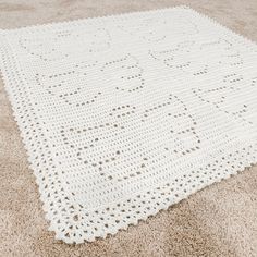 a white crocheted blanket laying on top of a carpeted floor with no one around it