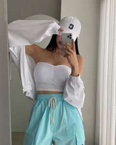 a woman taking a selfie in front of a mirror wearing shorts and a hat