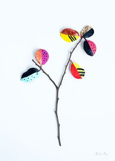 a branch with leaves painted on it and some dots in the middle, sitting against a white background