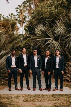 a group of men standing next to each other in front of palm trees and bushes