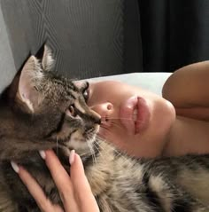 a woman laying on top of a bed next to a brown and black cat with her eyes closed