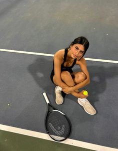 a woman sitting on the ground with a tennis racket and ball in her hand