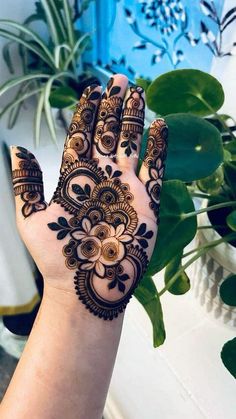 a woman's hand with henna on it and some plants in the background