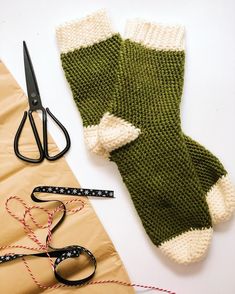 a pair of green and white knitted mitts next to scissors, measuring tape and thread