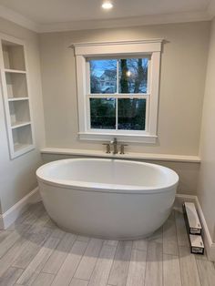 a large white bath tub sitting next to a window in a room with wooden floors