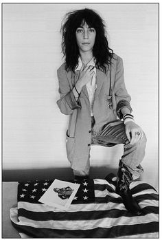 a black and white photo of a woman sitting on top of an american flag with her hands in her pockets