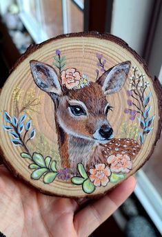 a hand holding a piece of wood with a deer painted on it