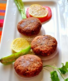 three small sandwiches on a white plate with asparagus and lemon wedges next to them