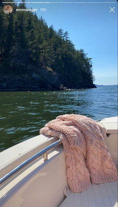 a pink blanket on the back of a boat in front of an island with trees