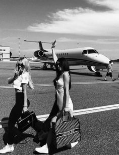 black and white photograph of two women walking towards an airplane with luggage on the tarmac