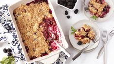 blueberry cobbler in a white dish with fresh berries on the side and two plates next to it