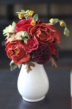 a white vase filled with red and yellow flowers