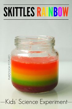 a jar filled with rainbow colored liquid sitting on top of a white table next to the words skittles rainbow