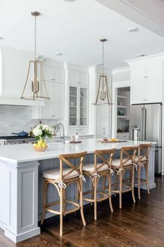 a large kitchen with white cabinets and wooden floors, along with an island that has four bar stools