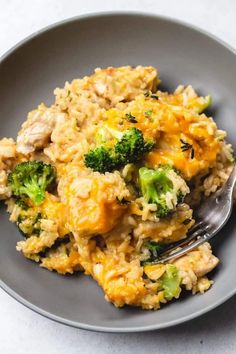 a gray plate topped with rice and broccoli covered in cheese sauce next to a fork