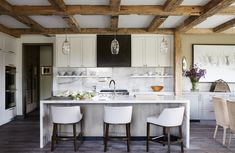 a large kitchen with white cabinets and wooden beams on the ceiling, along with two bar stools