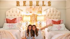 two women sitting on the floor in front of twin beds with pink and white bedding