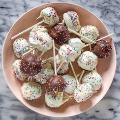 chocolate covered cake pops with sprinkles on a pink plate sitting on a marble table