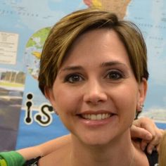 a woman with short hair smiling at the camera while holding onto her child's shoulder