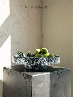 a bowl filled with green apples sitting on top of a cement block next to a wall