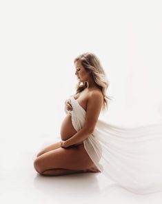 a pregnant woman sitting on the floor with her long white veil flying in the air