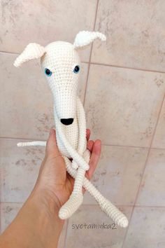 a crocheted white dog with blue eyes is held up by someone's hand