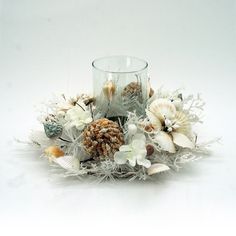 an arrangement of seashells and pineconis in a glass vase with a candle