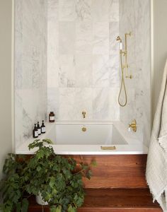 a bathroom with white marble walls and wooden flooring, along with a plant in the corner