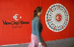 a woman walking past a red wall with a circular painting on it's side