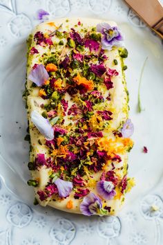 a piece of cake on a white plate with purple and orange flowers next to it