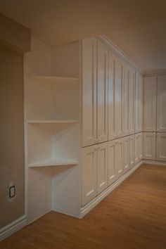 an empty room with white cabinets and wood flooring is pictured in this image, there are no people or objects on the shelves