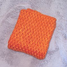 an orange crocheted blanket laying on top of a bed