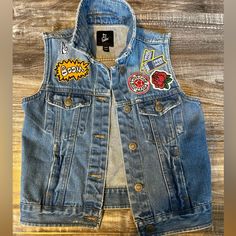 a denim vest with patches on the front and back, sitting on a wooden surface