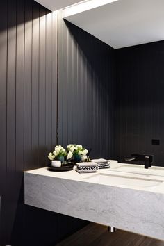 a bathroom with black walls and marble counter tops, white sinks and flowers in vases