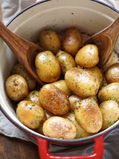 a red pot filled with potatoes on top of a wooden table next to a spoon