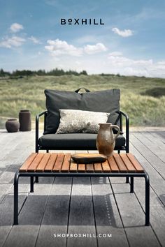 An outdoor lounge chair with dark gray cushion and black frame with a wooden top outdoor lounge table set on a wooden deck patio beside grassy field Wallpaper Fireplace, Work Chair, Outdoor Pendant Lighting, Bookcase Sideboard, Counter Height Table