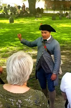 a man dressed in colonial clothing standing next to an older woman and pointing at something