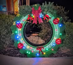 a lighted christmas wreath in the middle of a garden at night with lights on it