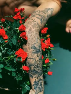 a person with tattoos on their arm holding a potted plant filled with red roses