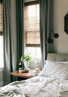 a bed with white sheets and pillows next to a window in a room that has gray drapes