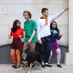 four people and a dog are standing in front of a building with their arms up