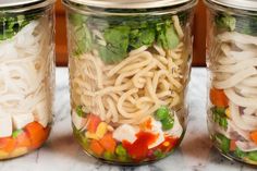 three mason jars filled with different types of pasta and veggies in them on a marble counter top